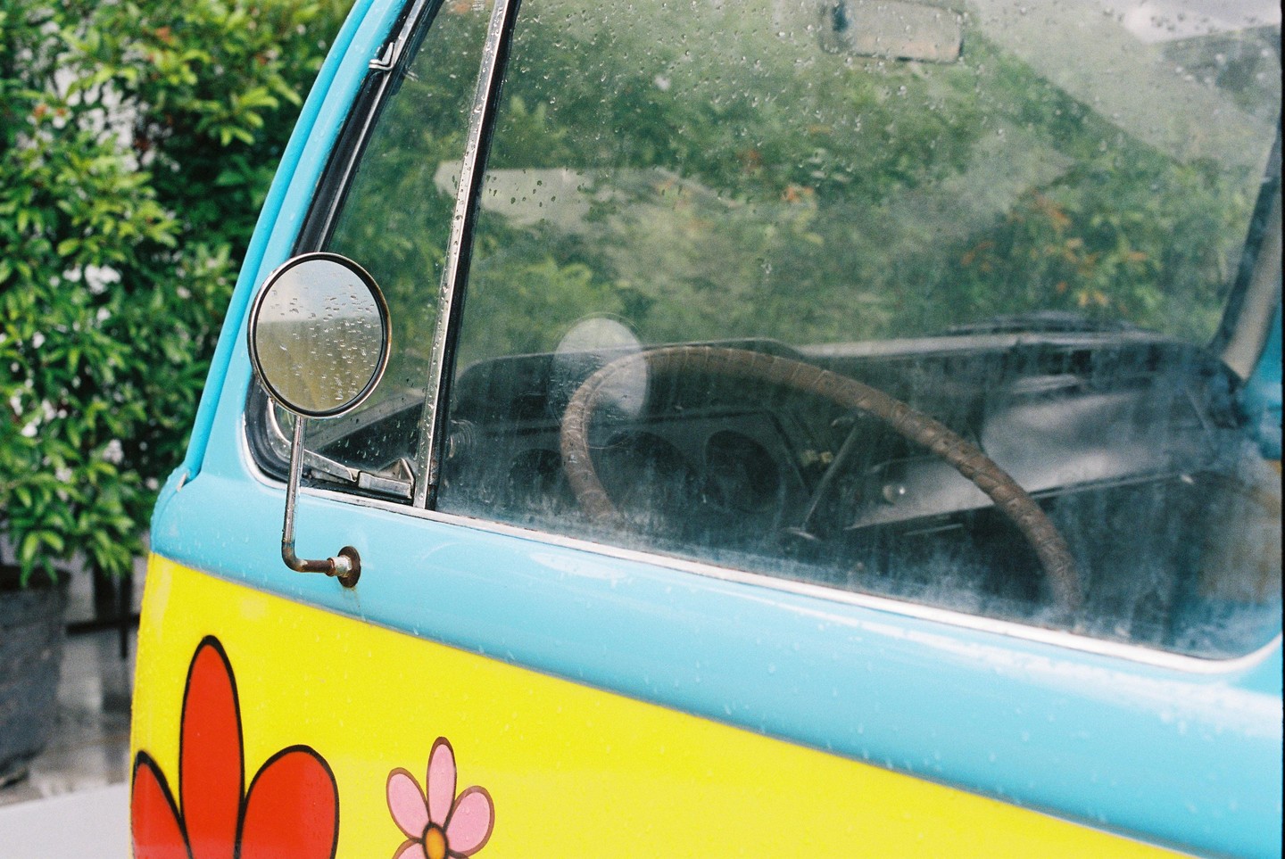 A blue and yellow van with flower decals is covered in raindrops, with the steering wheel visible through the wet windshield.