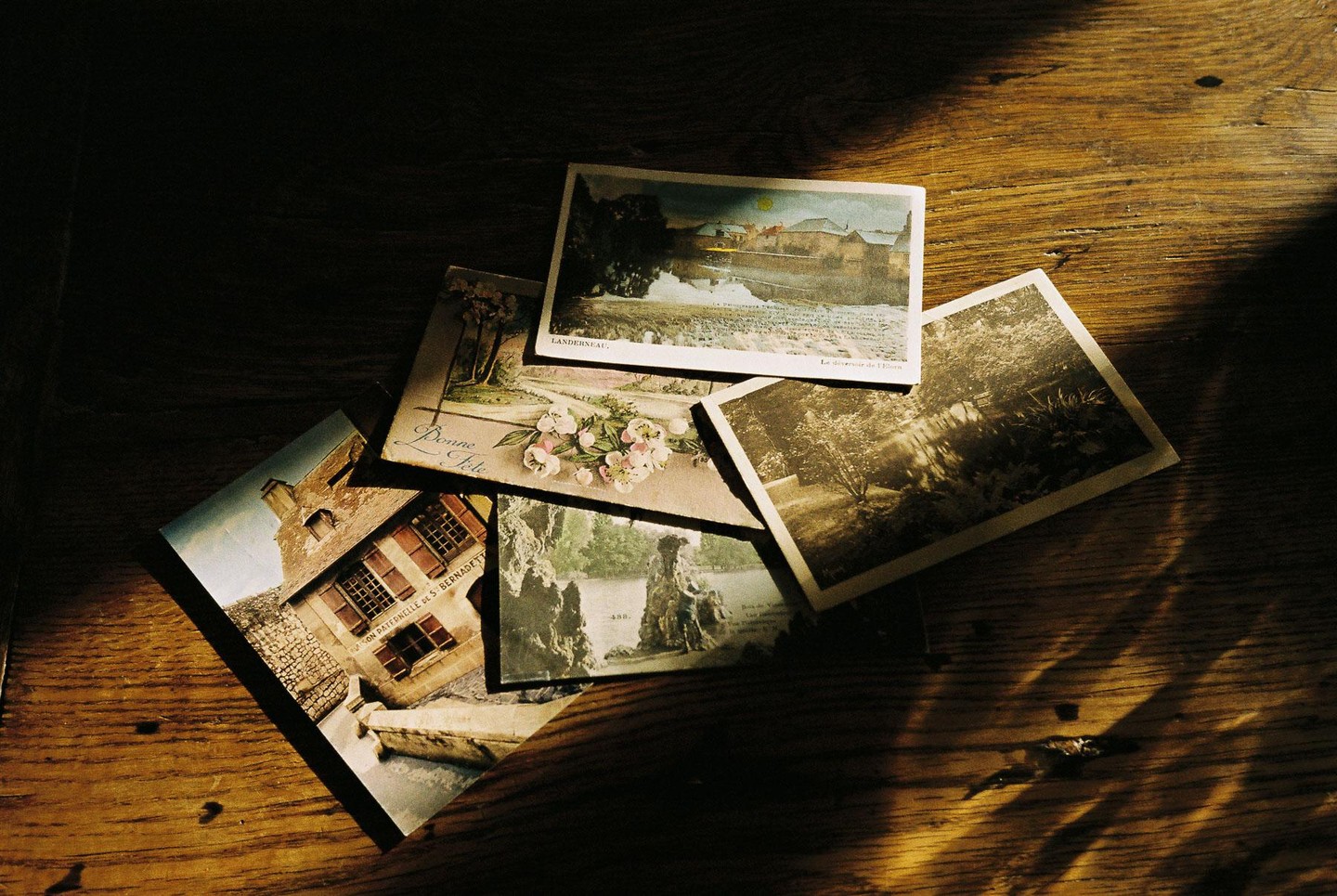 Several vintage postcards are scattered on a wooden surface, illuminated by a strong diagonal beam of light.