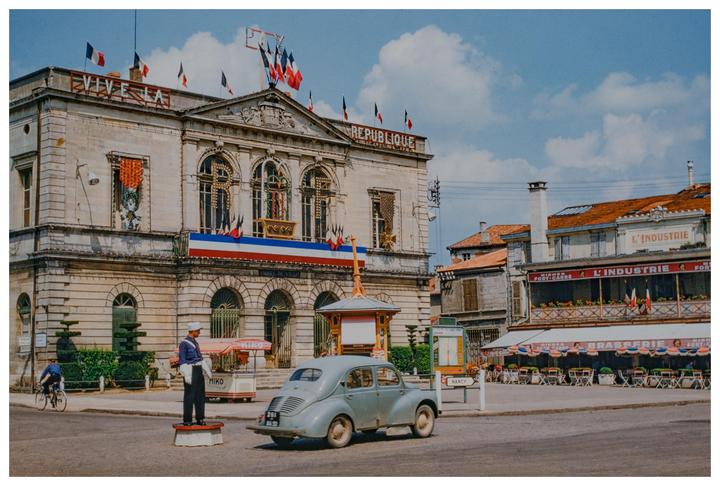 A street scene in France shows a building with "REPUBLIQUE" written on it, a vintage car, and a man on a bicycle.