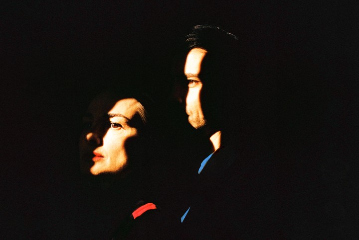 A woman and a man are illuminated by strong, contrasting light and shadow.