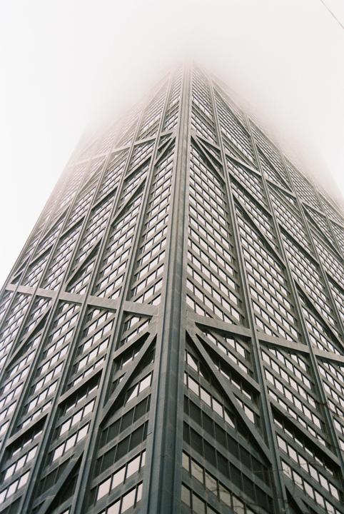 A tall skyscraper with a grid pattern of windows disappears into a hazy sky.