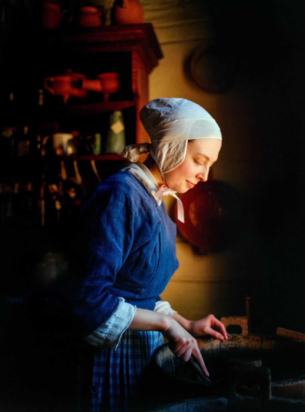 A woman in historical attire is working in a dimly lit room.