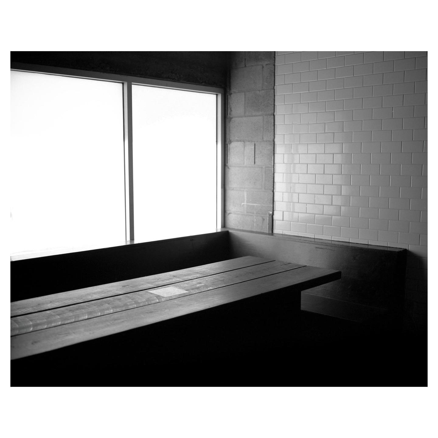 A wooden table and bench are next to a window and a tiled wall.