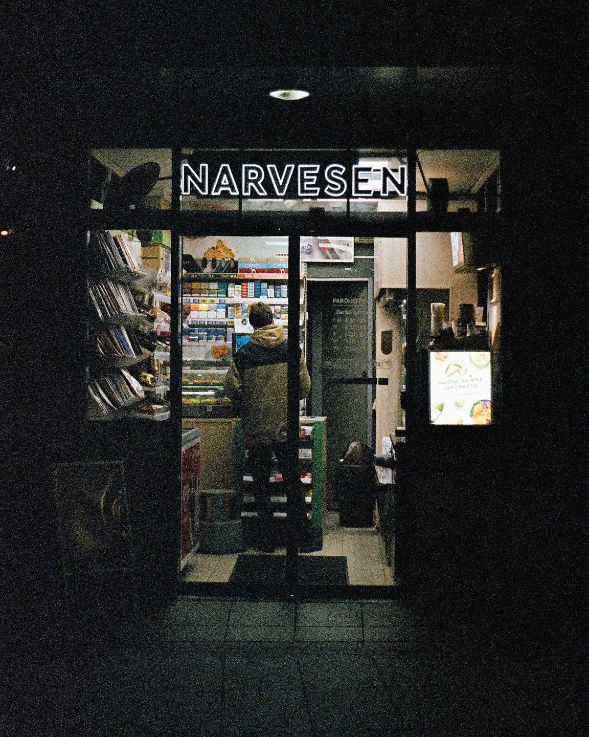 A man stands inside a brightly lit Narvesen convenience store at night.