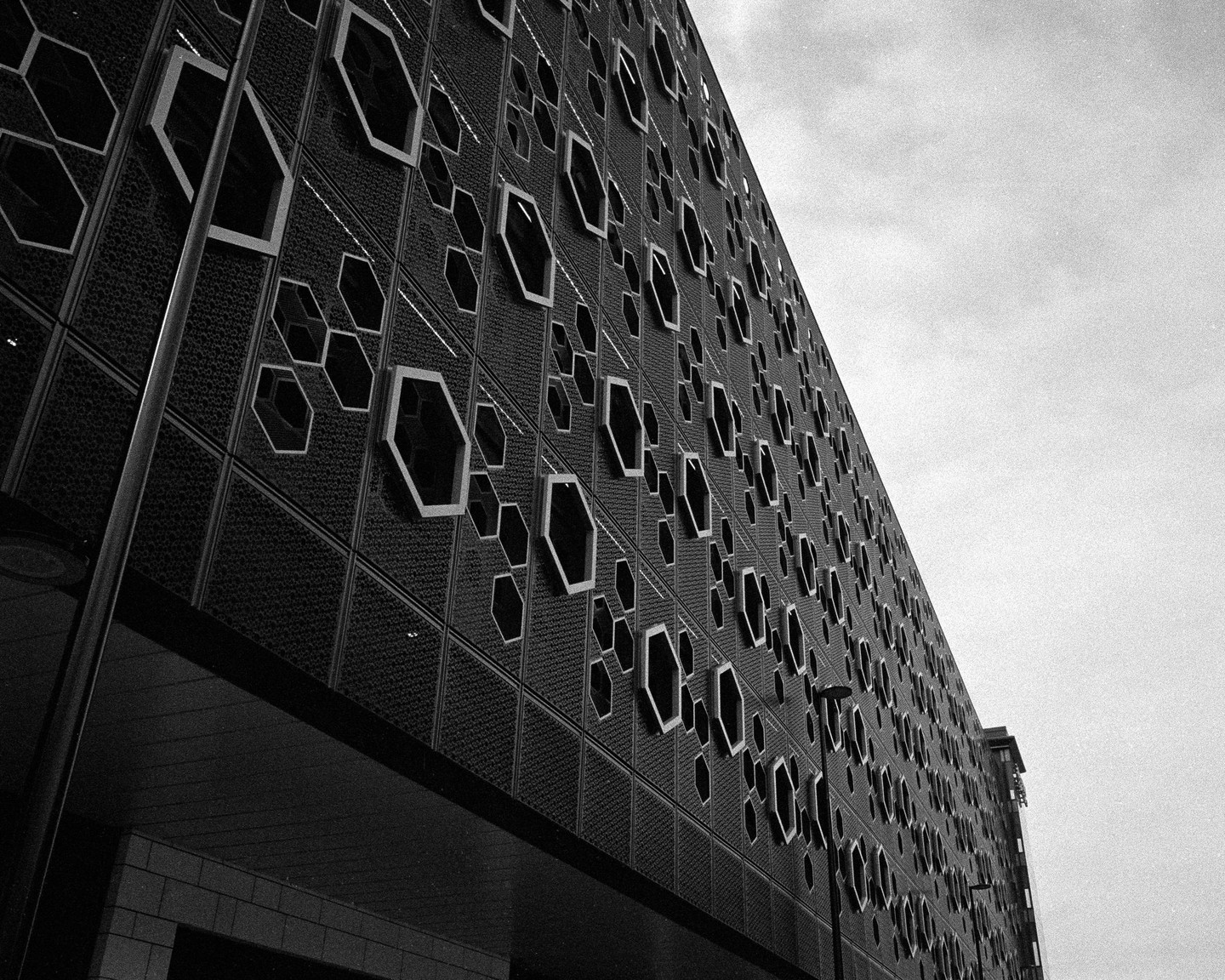 A building with a facade of hexagonal windows is seen from a low angle against a cloudy sky.