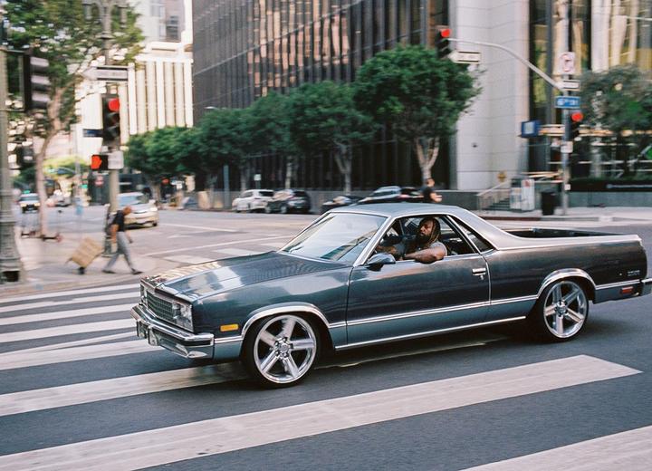 A man drives a classic car across a crosswalk in a city.