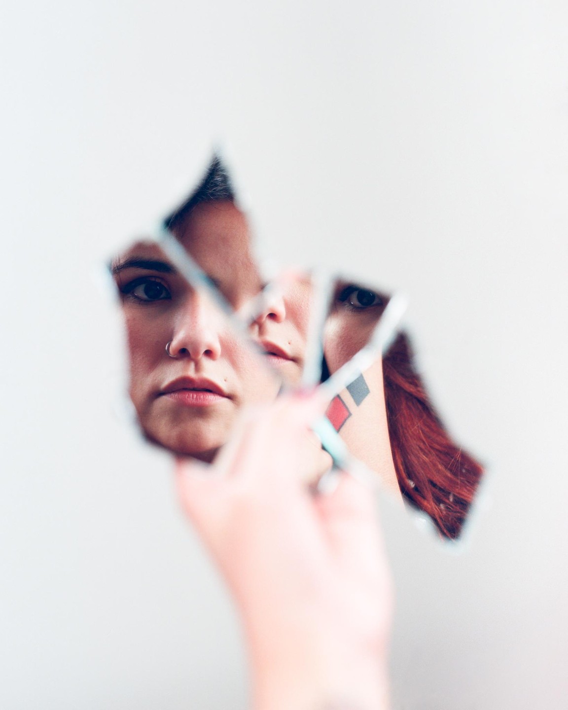 A woman's face is reflected in pieces of a broken mirror held by a hand.