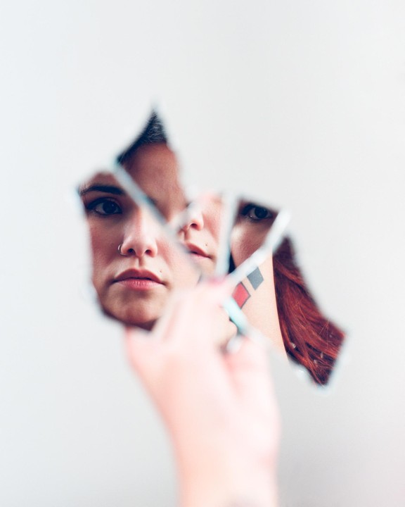 A woman's face is reflected in pieces of a broken mirror held by a hand.
