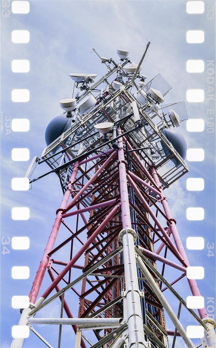 A low-angle view shows a red and white communications tower against a blue sky.