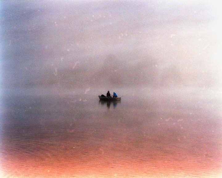 Two people in a small boat are on a body of water under a hazy sky.