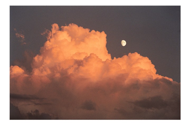 The moon is visible above a large orange cloud at sunset.