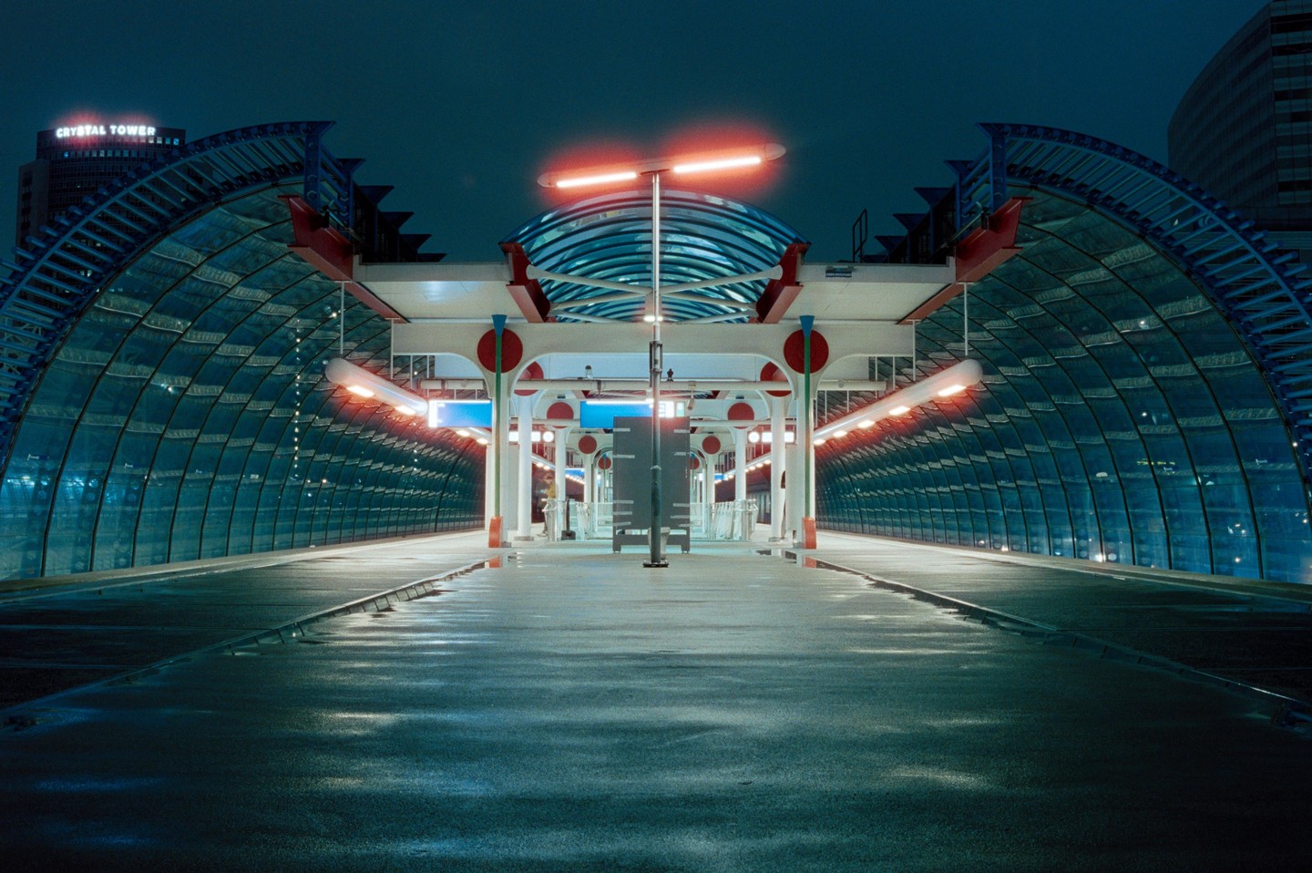 A modern, empty train station platform is illuminated by orange and blue lights at night.