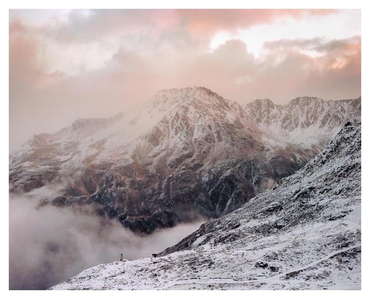 Snow-covered mountains are partially obscured by clouds under a pink sky.