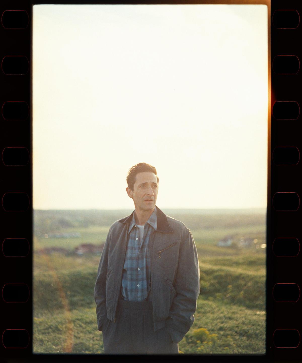 A man stands in a field at sunset, looking towards the right.
