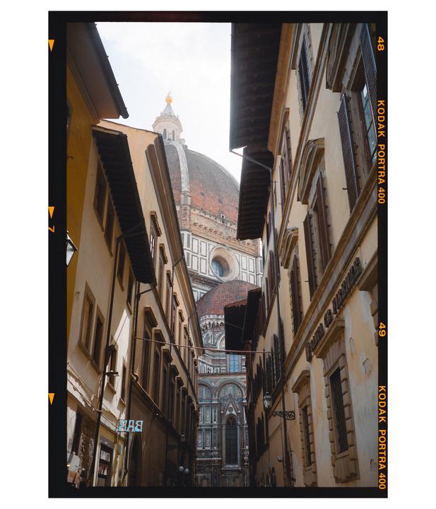 A narrow street leads to a large domed building in a city.