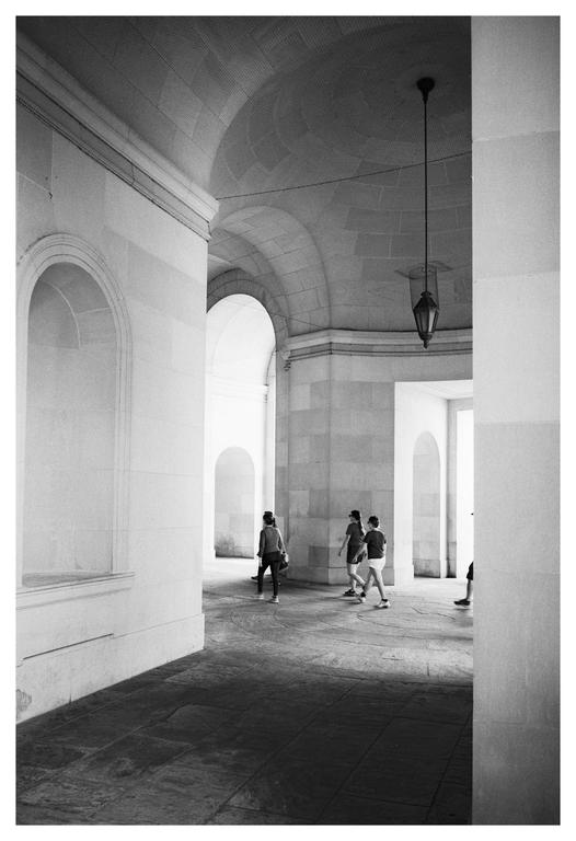 Three people walk through a stone corridor with arched doorways and a hanging lantern.