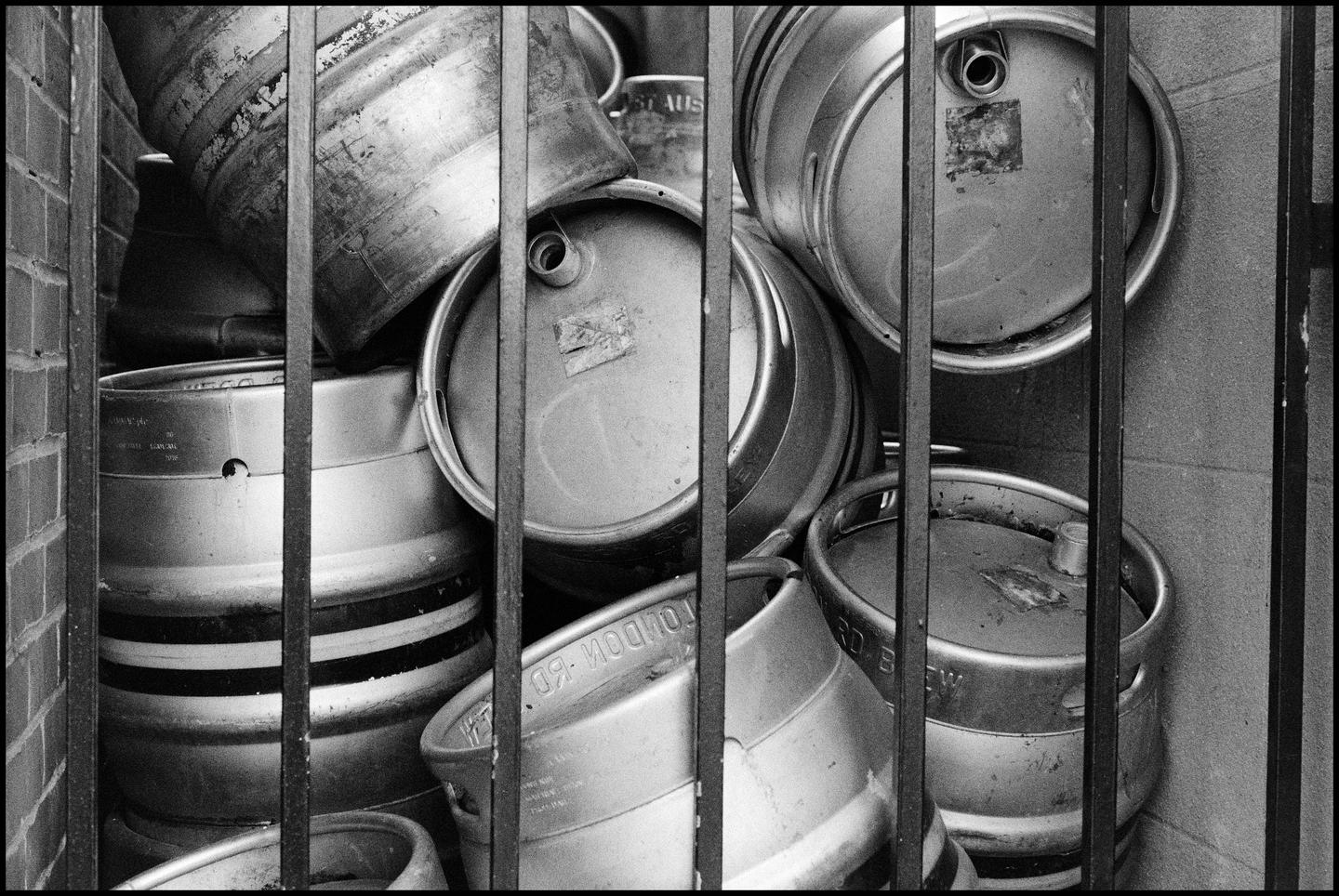 A pile of beer kegs is visible behind a metal fence.