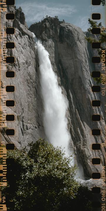 A large waterfall cascades down a rocky cliff face with green trees in the foreground.
