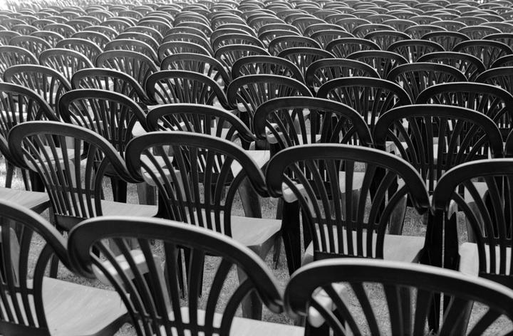 Many rows of empty chairs are arranged on a grassy field.