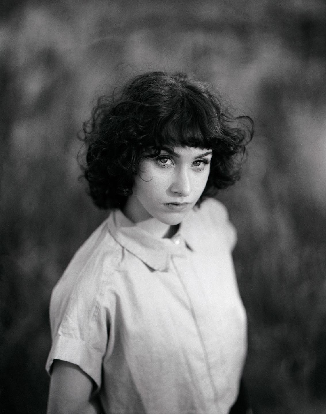 A woman with curly hair and bangs looks directly at the viewer.