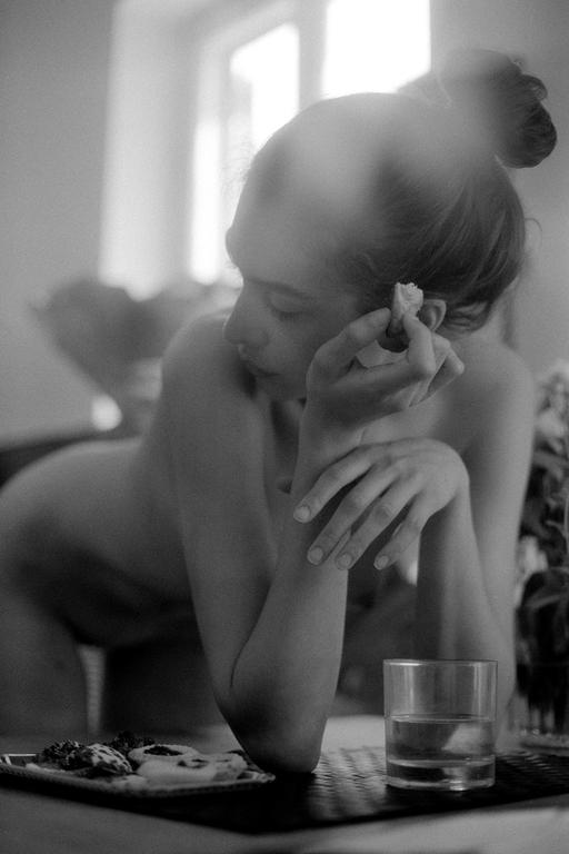 A woman with her hair in a bun leans on a table with a glass of water and a plate of cookies.