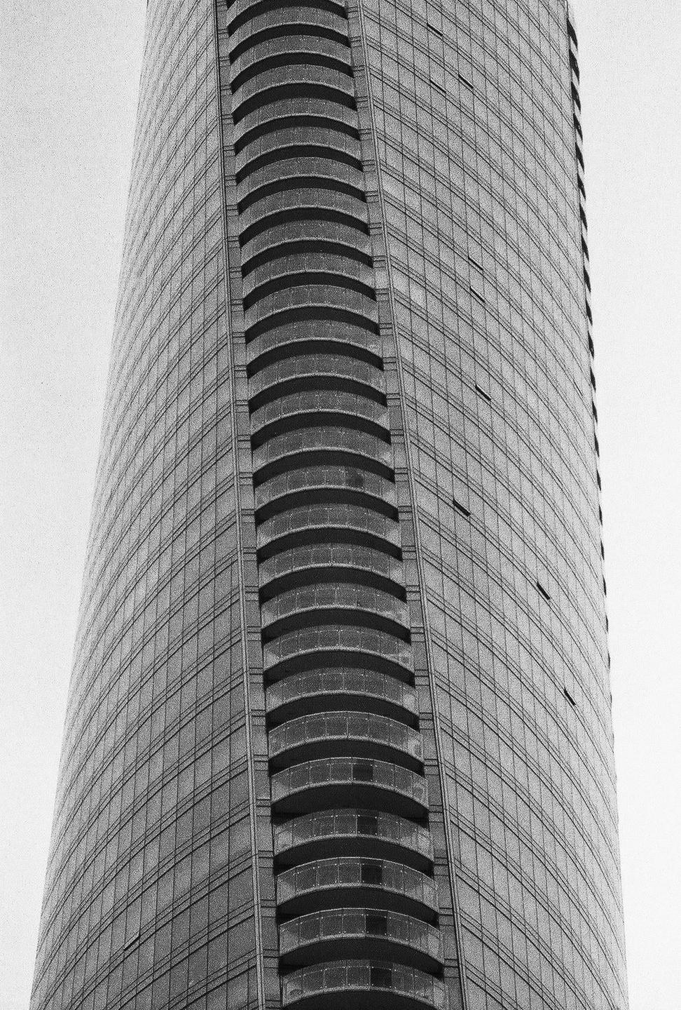 A tall building with many windows and curved balconies is shown from a low angle.
