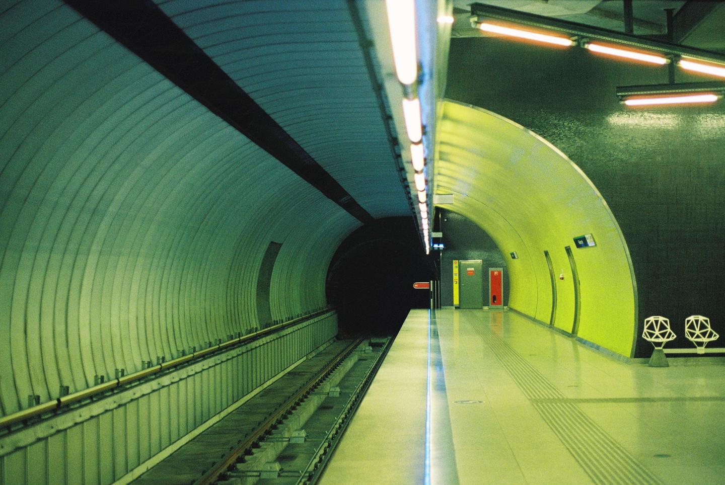A subway platform and tracks are visible in a long, curving tunnel with bright yellow and green walls.