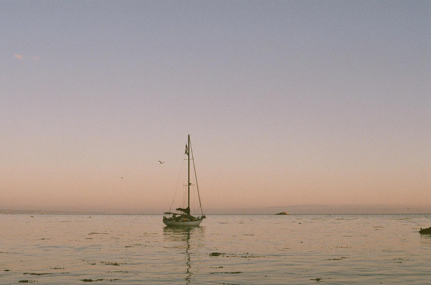 A sailboat floats on calm water under a pastel sky at sunset.