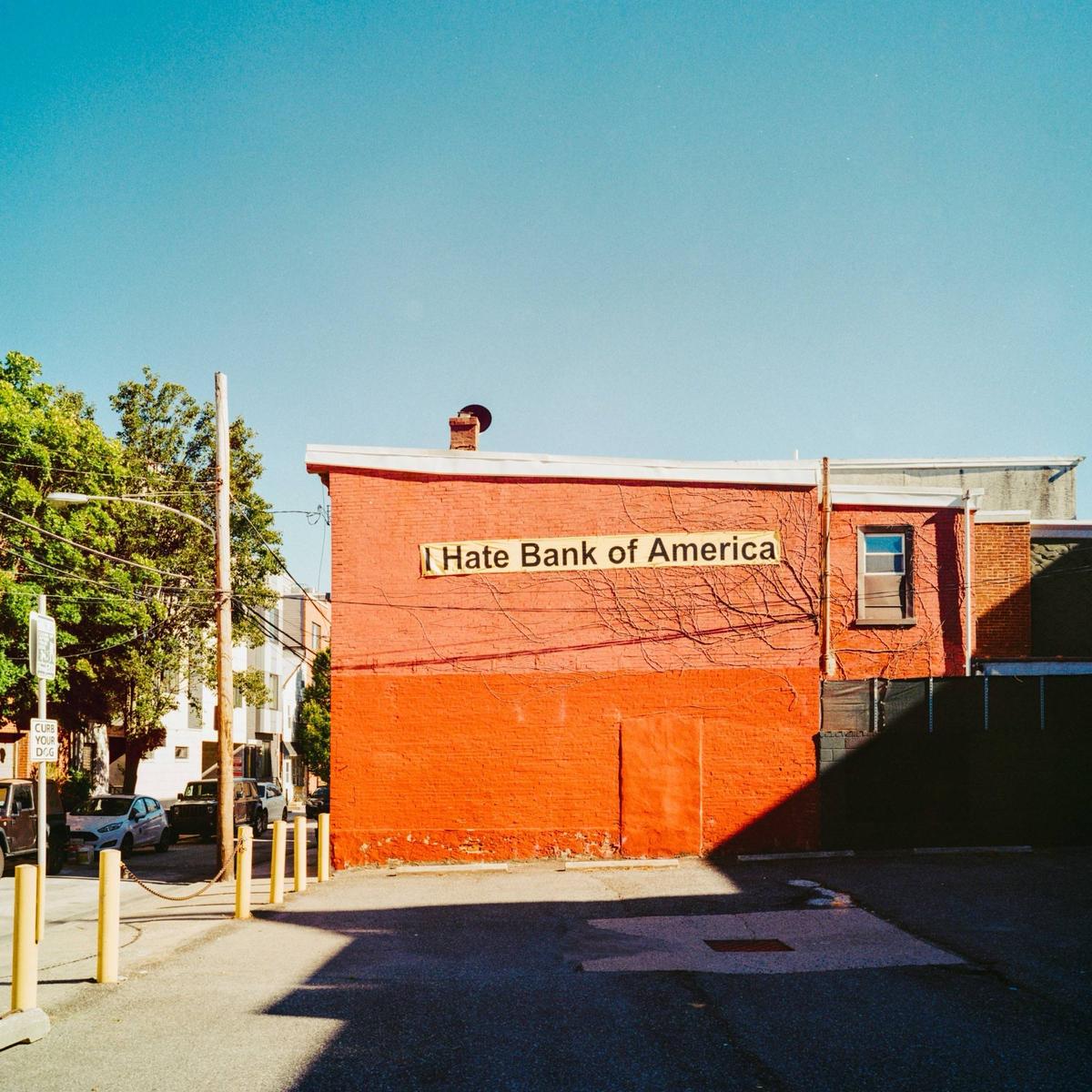 A red brick building with a sign that reads "I Hate Bank of America" is visible from a parking lot.