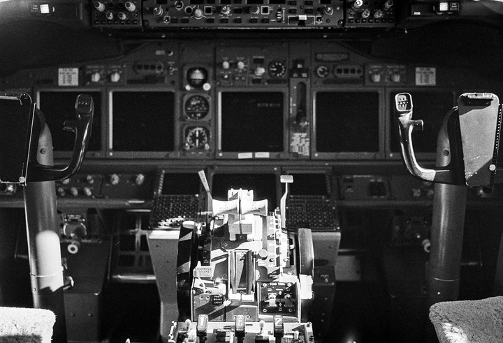 The cockpit of an airplane is visible, showing the control panel, steering yokes, and throttle.