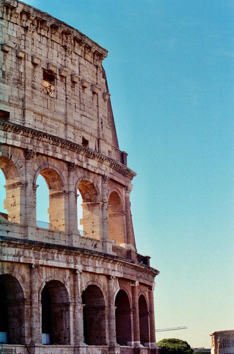 The Colosseum in Rome is visible from a low angle, with a clear blue sky in the background.