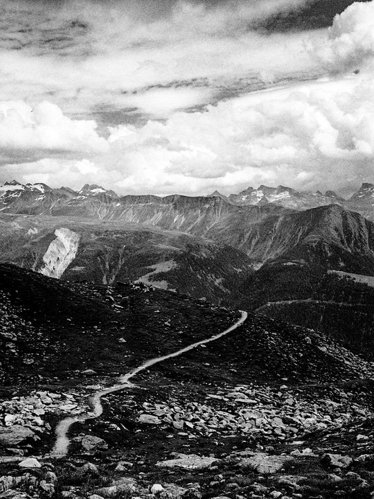A winding path leads through a rocky mountain landscape under a cloudy sky.