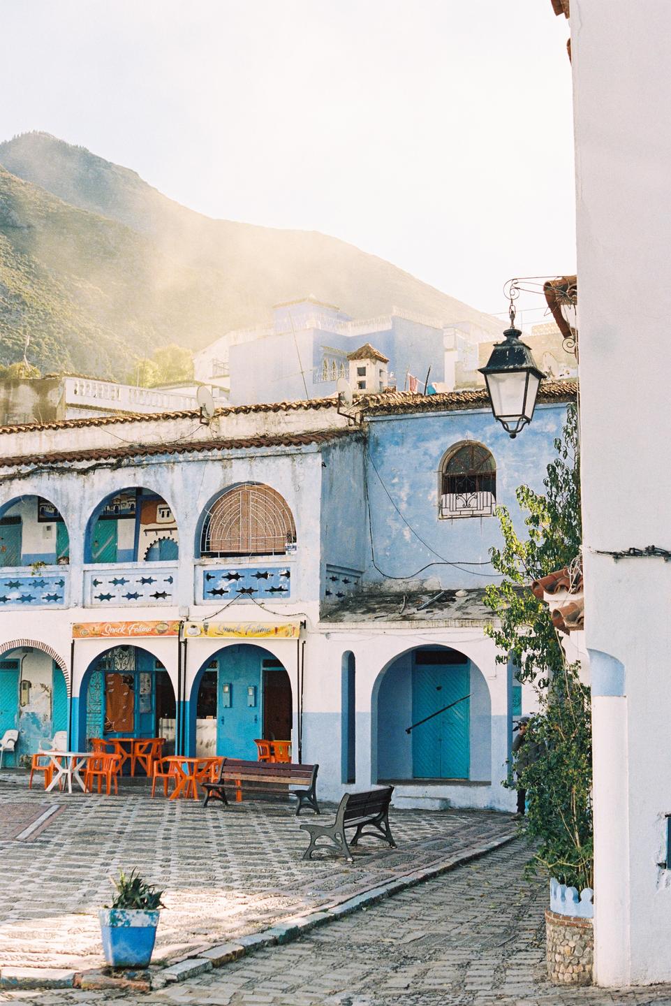 A street in a blue city with mountains in the background.