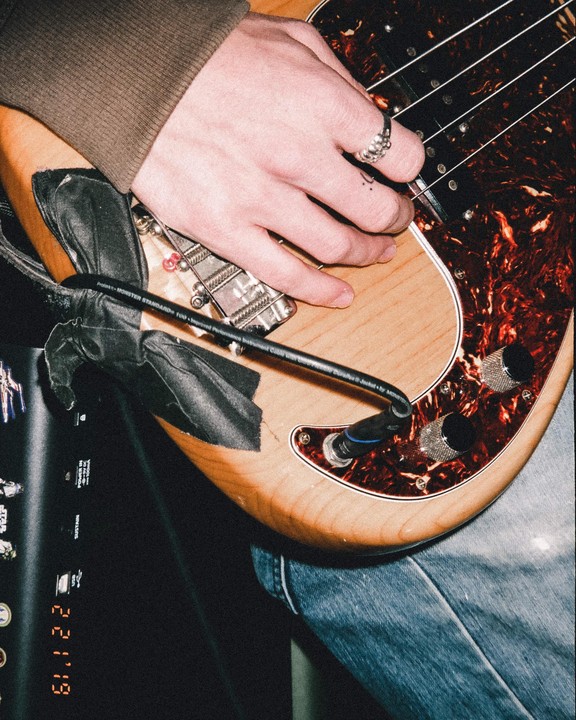 A person's hand with a ring is playing a bass guitar with a tortoiseshell pickguard.
