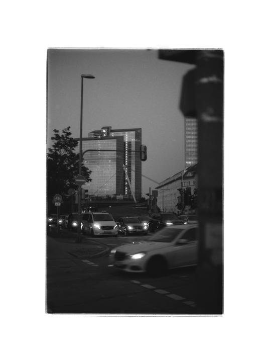 A street scene at dusk shows cars with illuminated headlights and a tall building in the background.