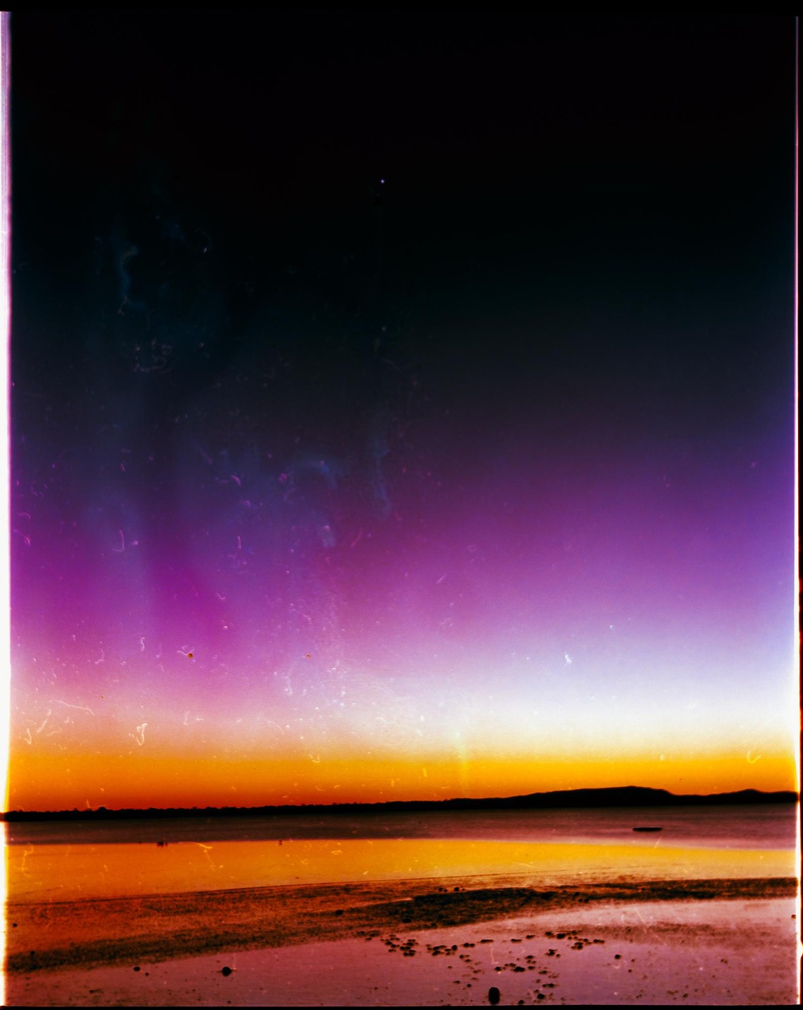 A vibrant sunset over a body of water with a distant landmass.