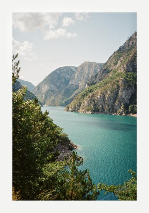 A body of turquoise water flows between two large mountains covered in trees.