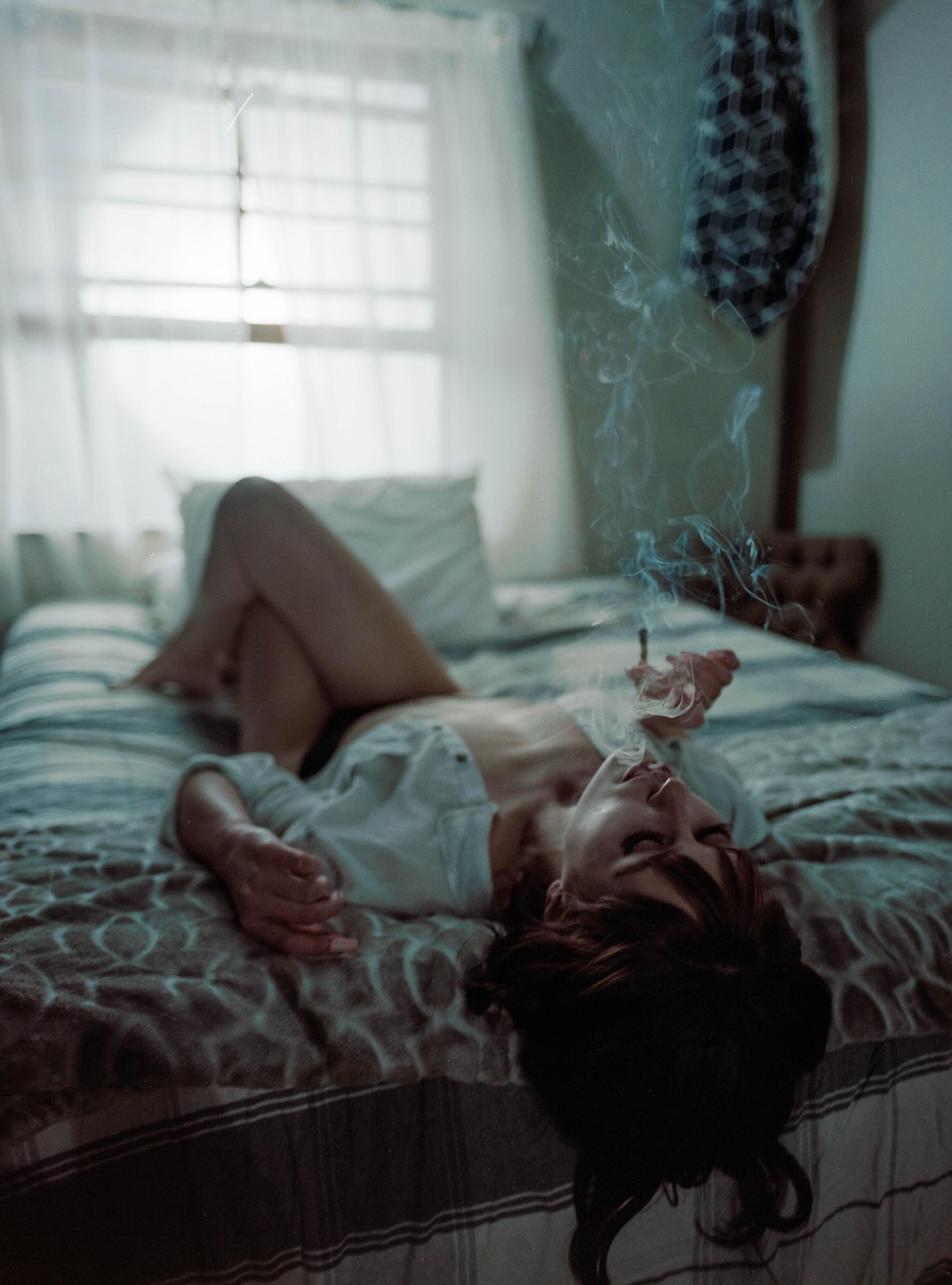 A woman lies on a bed, exhaling smoke from a cigarette.