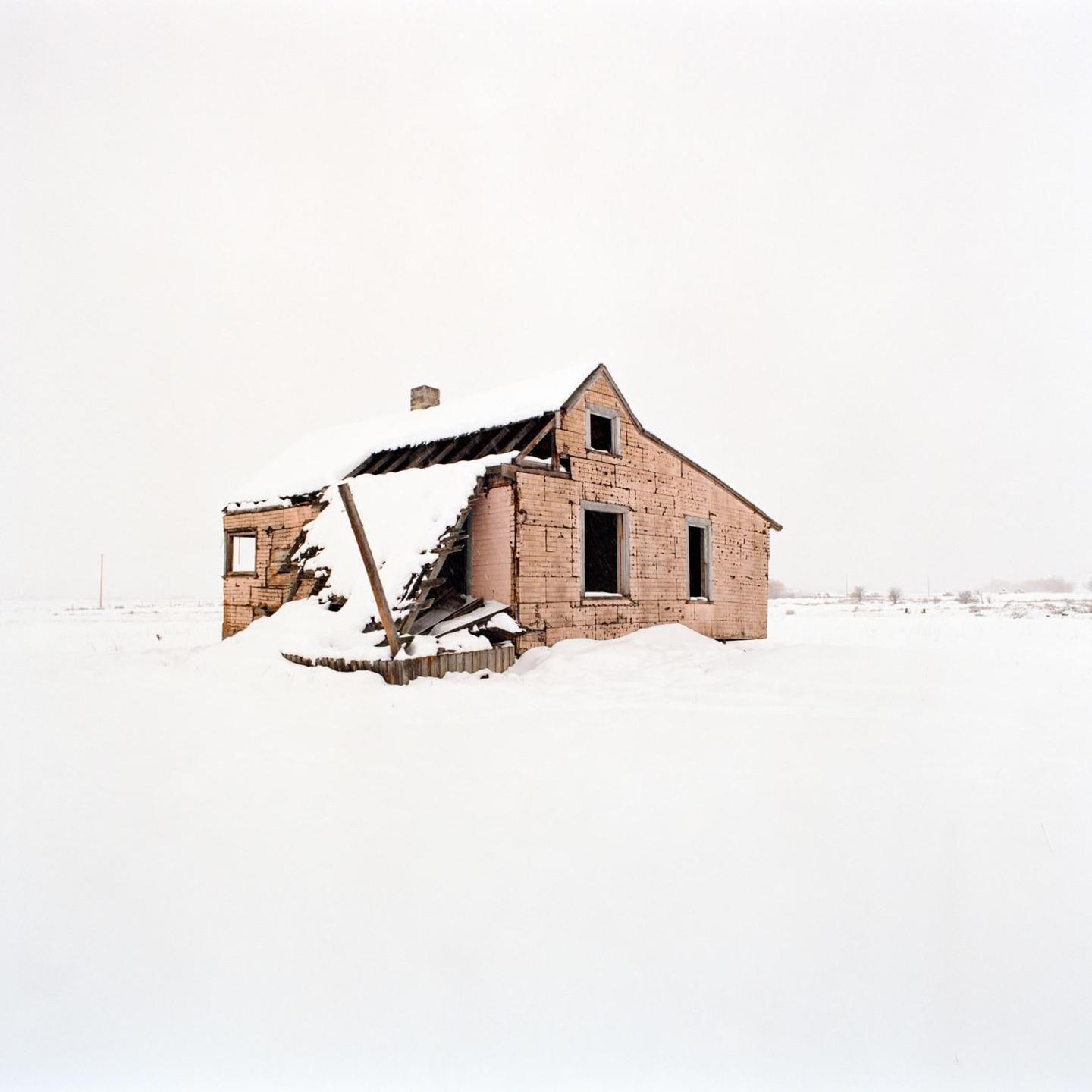 An abandoned house with a partially collapsed roof is covered in snow.