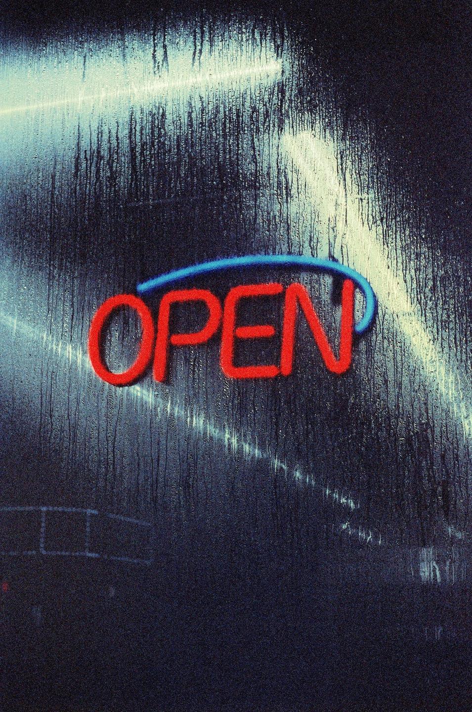 A neon sign that says "OPEN" is visible through a rain-streaked window at night.