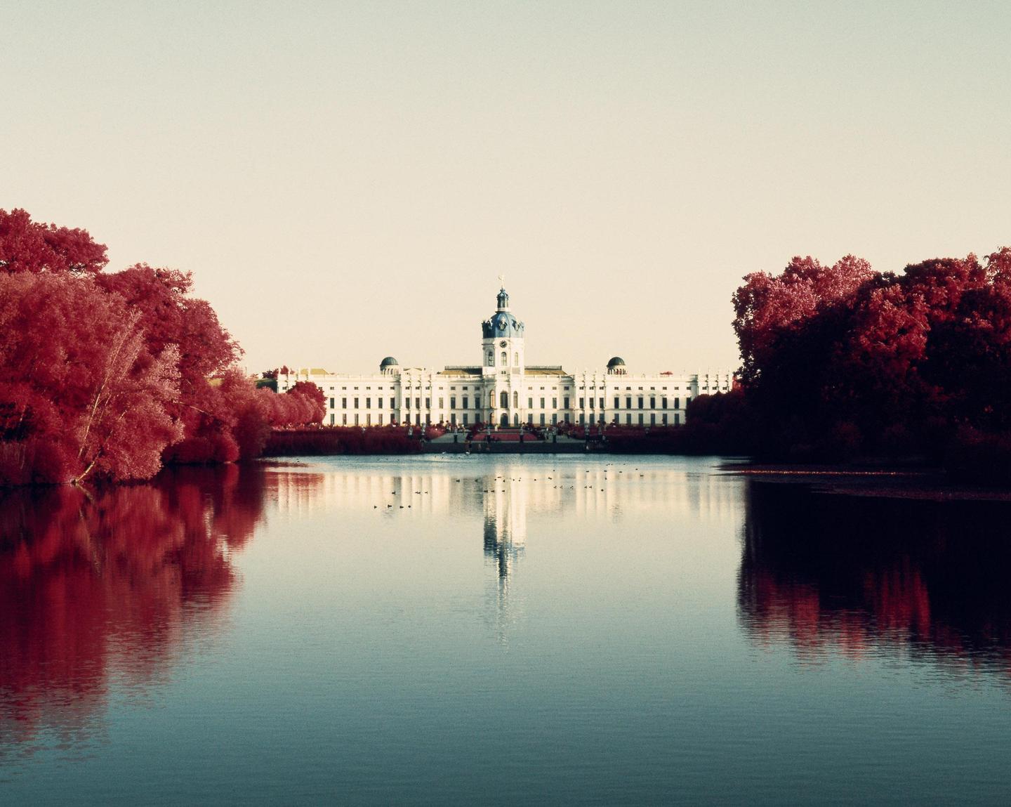 Charlottenburg Palace is reflected in the water, surrounded by red trees.