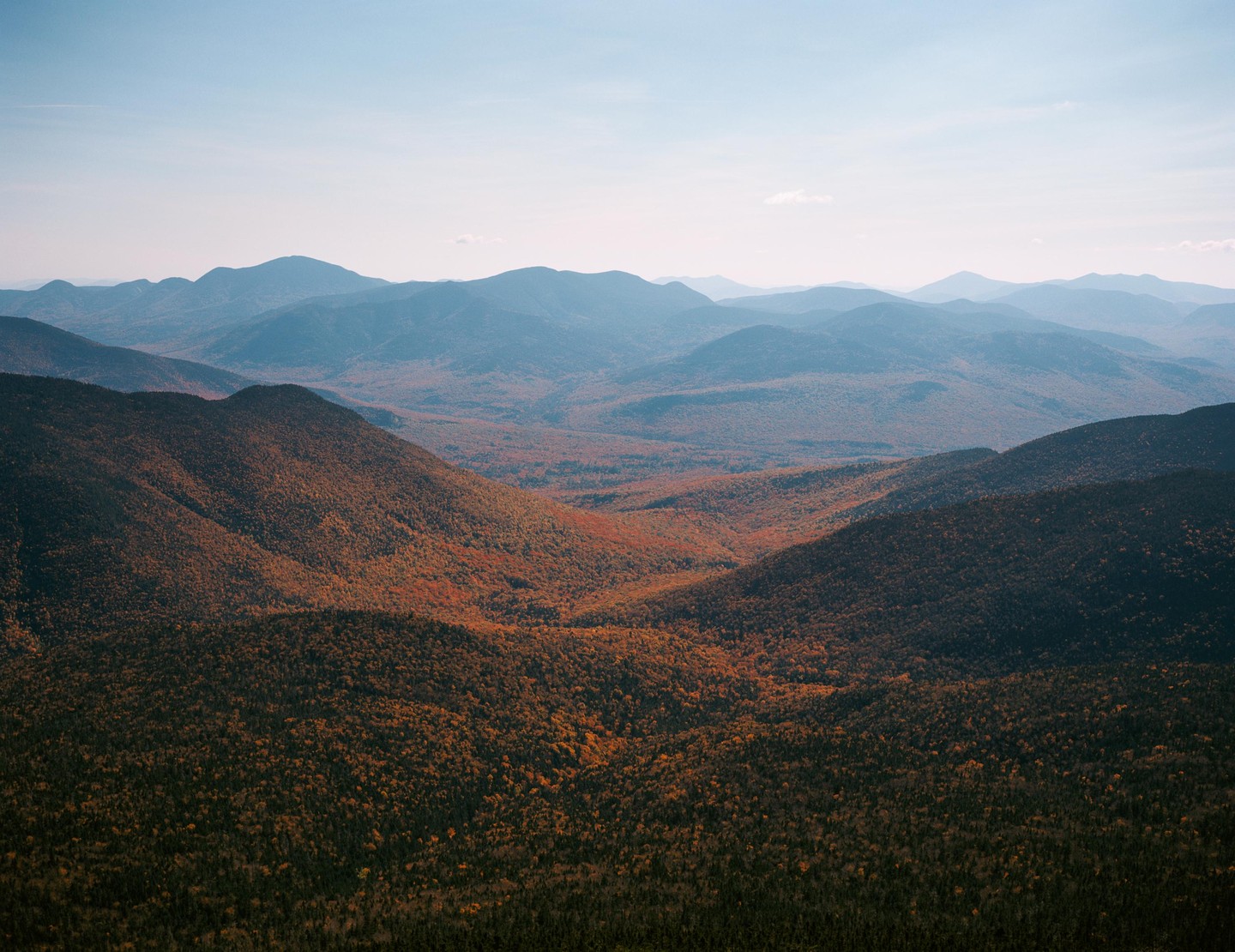 A vast mountain landscape is covered in autumn foliage under a clear sky.