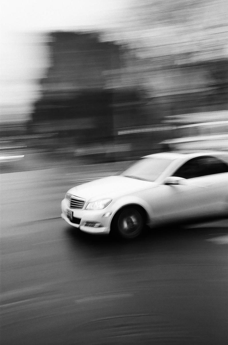 A white car speeds across a street with a blurred background.