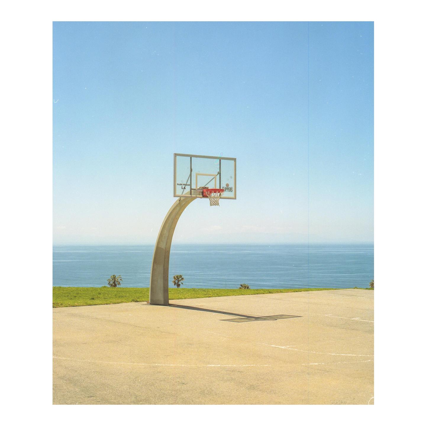 A basketball hoop stands on a court overlooking the ocean.