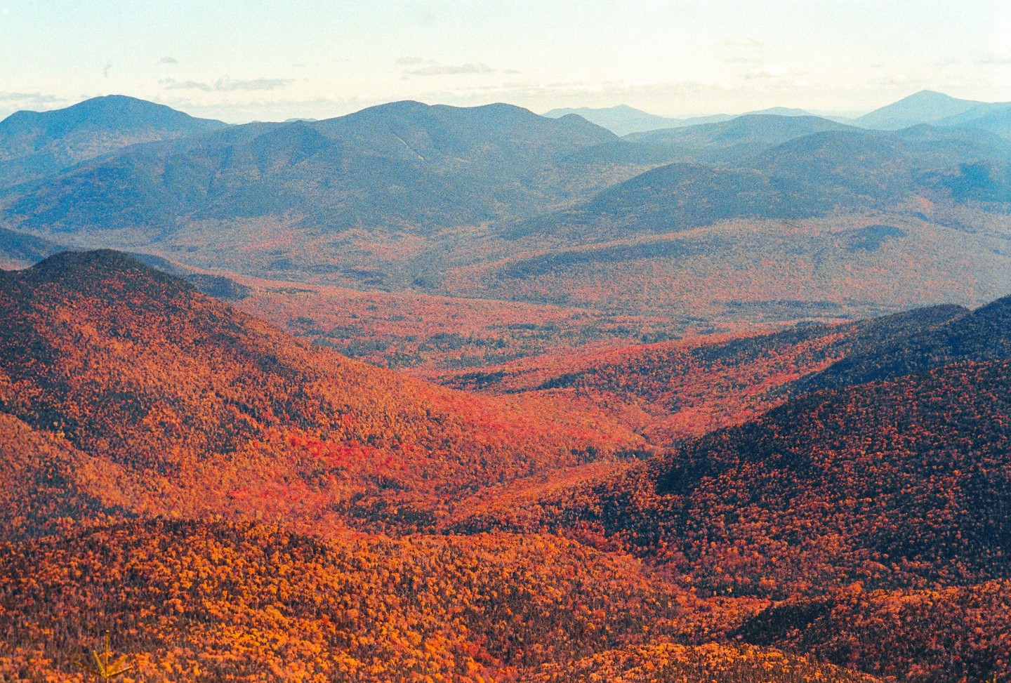 A vast mountain landscape is covered in autumn foliage under a bright sky.