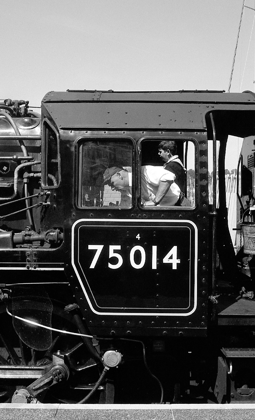 Two men are visible through the windows of a large train engine with the number 75014 on its side.