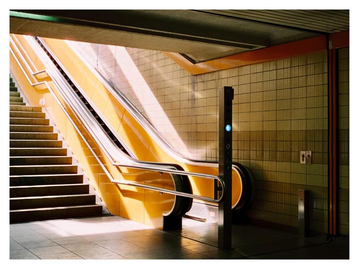 Sunlight illuminates an escalator and a staircase in a subway station.