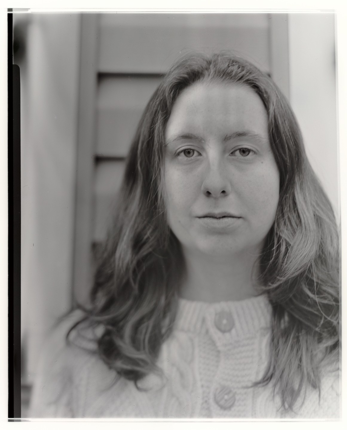 A woman with long hair and a cable-knit sweater looks directly at the viewer.