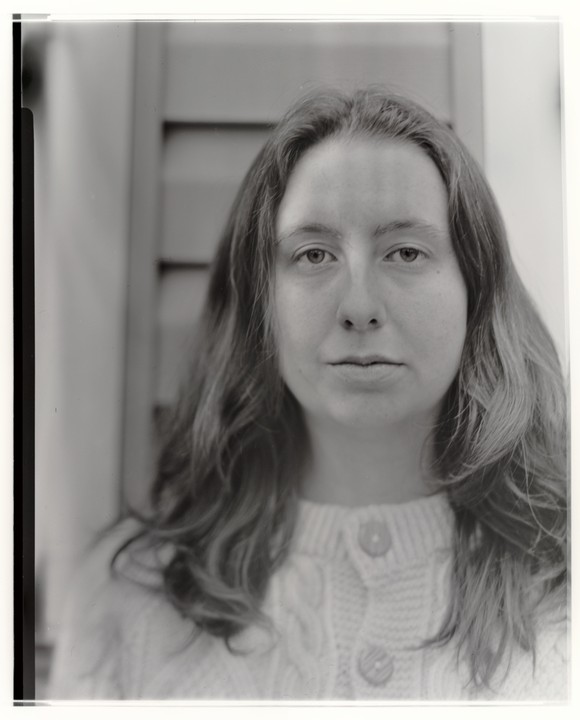 A woman with long hair and a cable-knit sweater looks directly at the viewer.