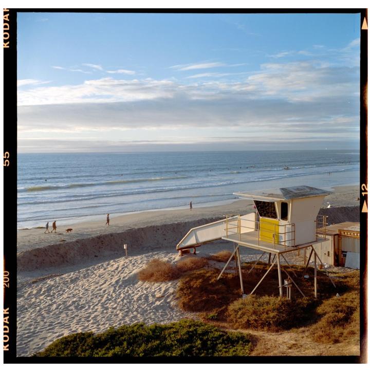 A lifeguard tower stands on a sandy beach next to the ocean under a partly cloudy sky.